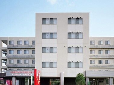 グレー系の5階建ての建物は頑丈な外観で、1階部分には屋根が付いている。屋外階段もあり、周辺には木も植えられている。