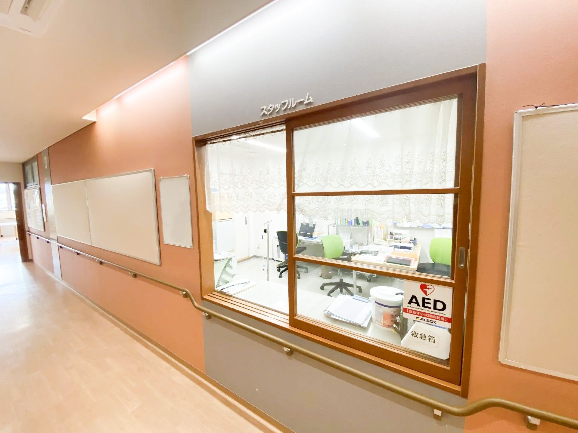 ライトグレーの5階建ての建物には屋外階段が設置され、クリニックも併設されている。周りには木も植えられている。