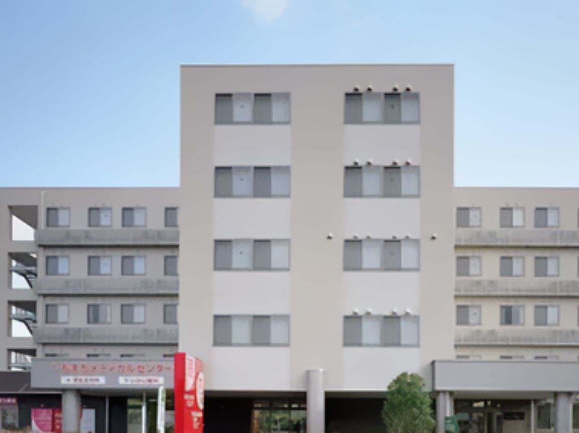 グレー系の5階建ての建物は頑丈な外観で、1階部分には屋根が付いている。屋外階段もあり、周辺には木も植えられている。