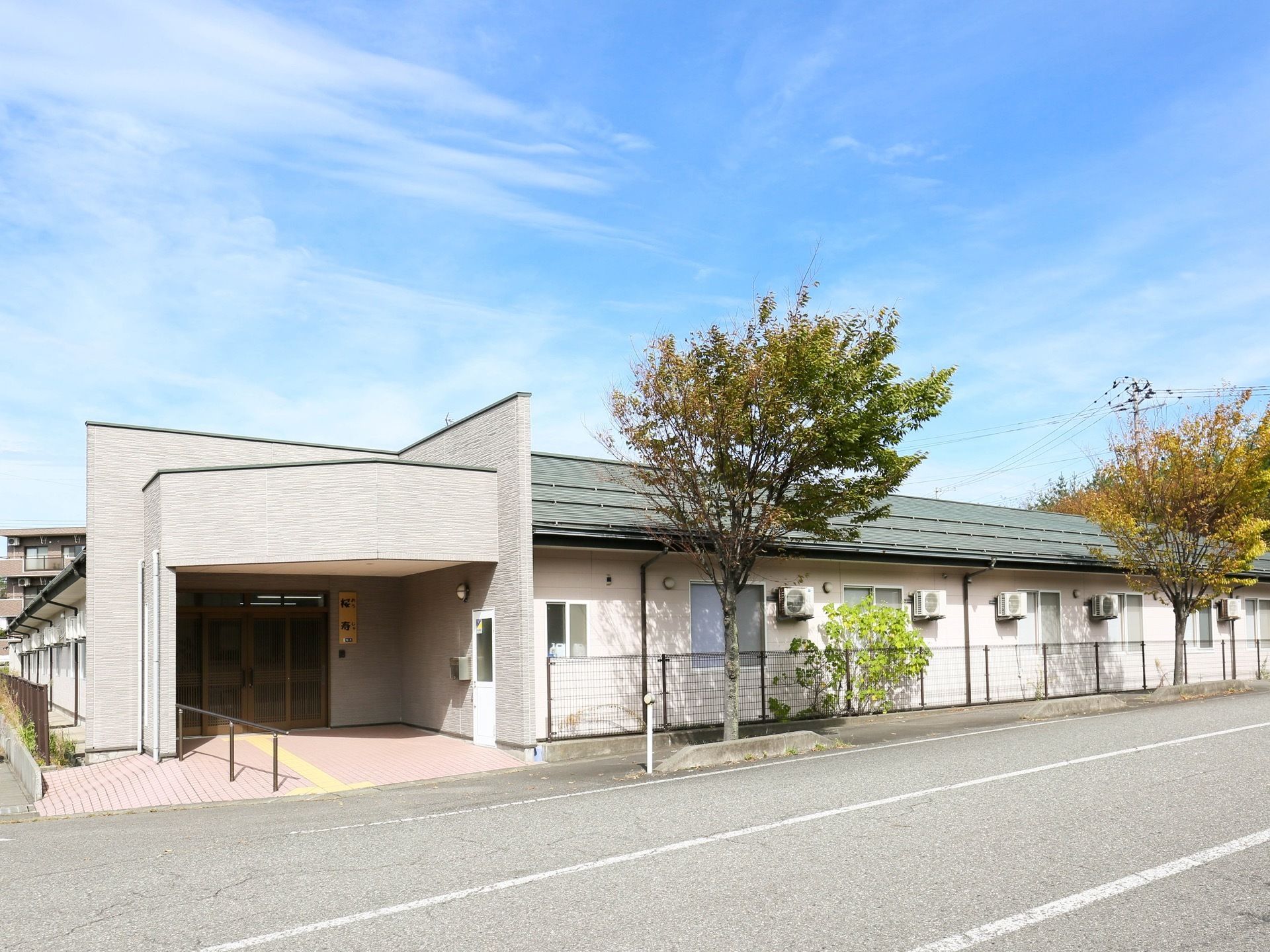 道路沿いの角地に、Ｌ字型の白い建物が建っている。安全のためエントランスを奥まった造りにして、道路から距離を取っている。