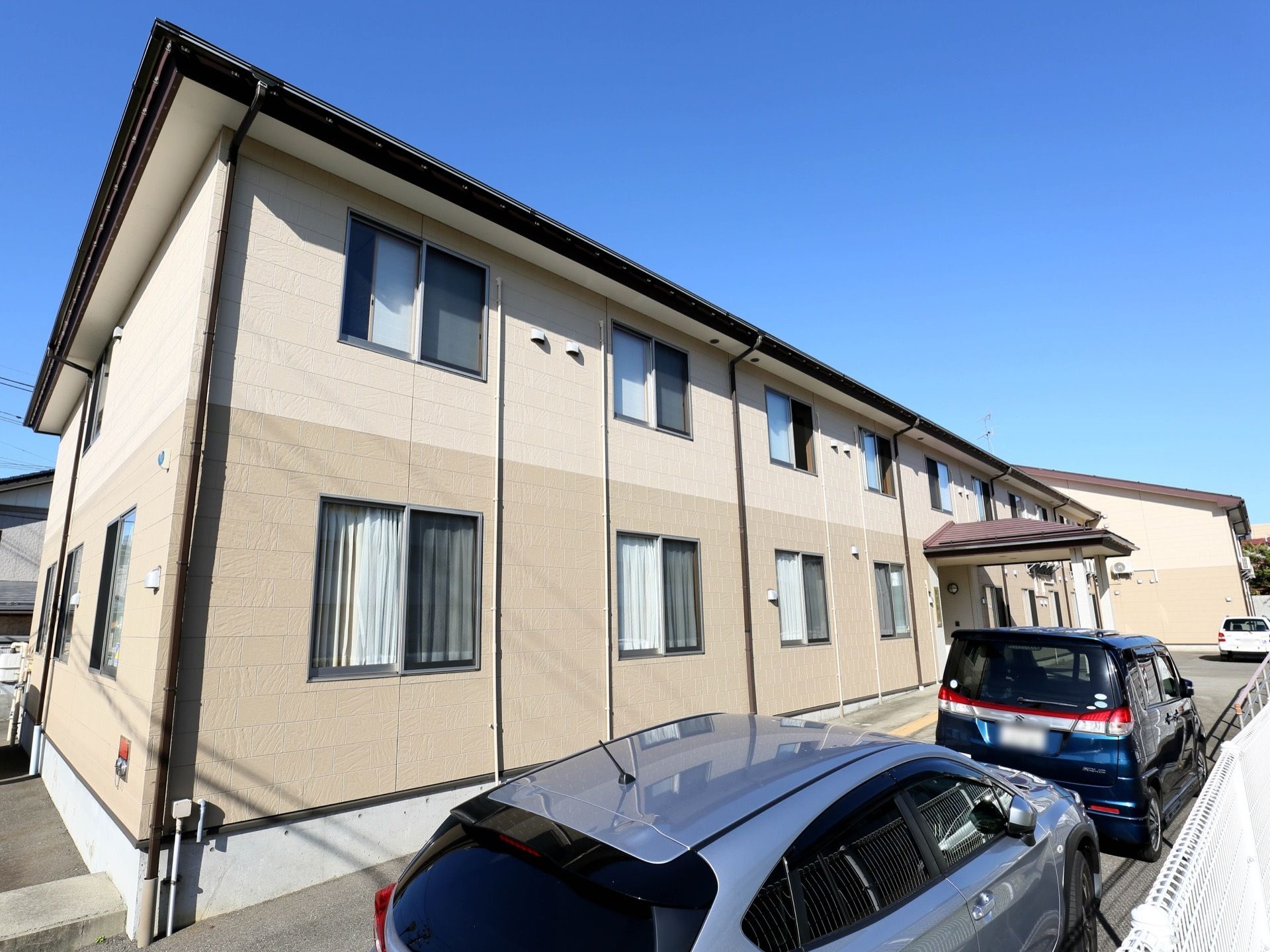 白とグレーのツートンカラーの外壁が柔らかい印象の外観。2階建てで、等間隔に複数の窓がある。