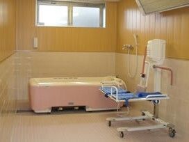 白とピンクの機械浴が一番奥に置かれた浴室。壁の上部にはパネルヒーターが設置され、その下にはリフトがある。