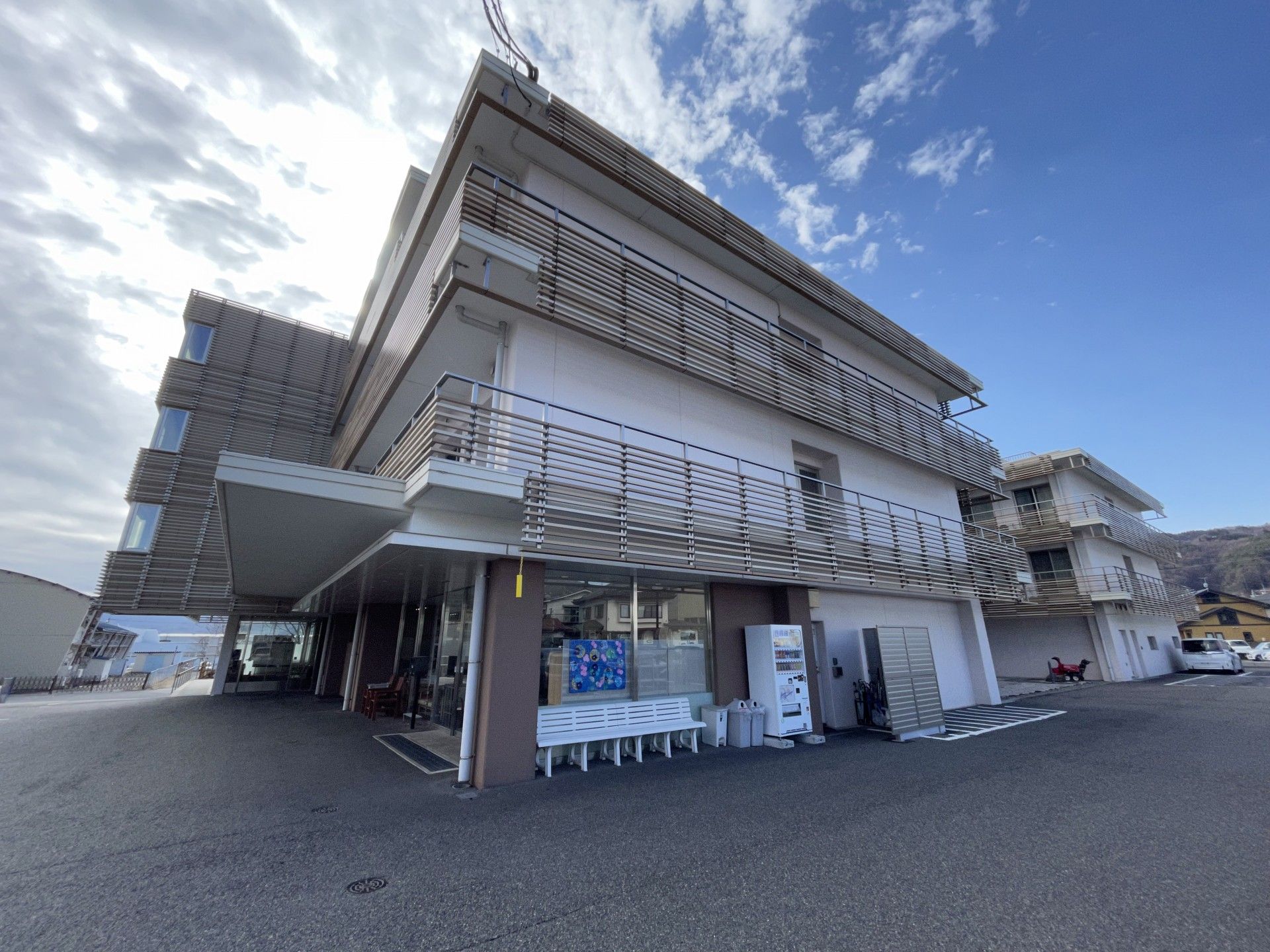 車いすの高齢女性と付き添いのエプロンを付けた女性スタッフが笑顔で屋外で過ごしている。