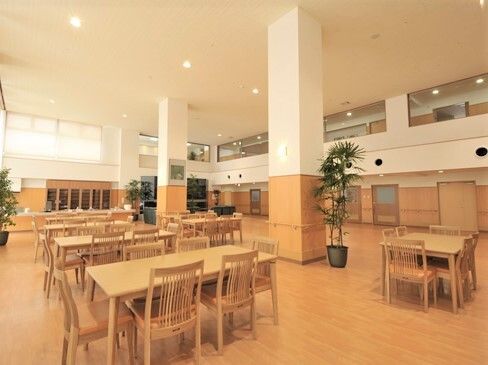 木製のテーブルと椅子が置いてある施設内のリビングスペース。天井が高い様子