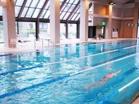 25ｍある室内のプールを独りの人が泳いでいる。プールの出入り口には手すりが付き、プールの周りにはいすが置かれている。
