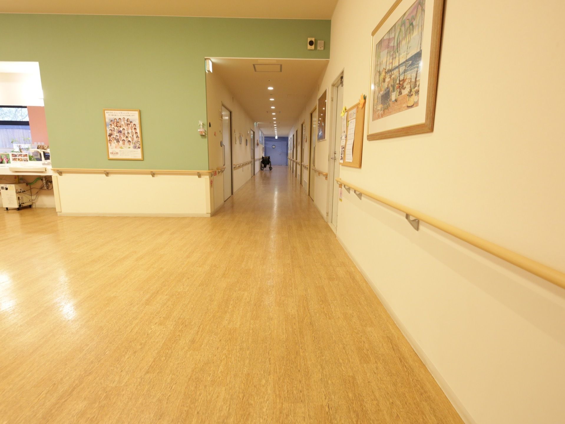 見通しのよい廊下である。居室入口以外の壁には手すりが設置されている。天井には多くの照明器具がついている。