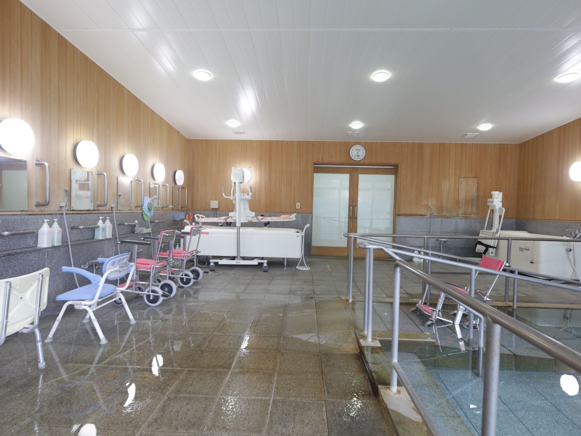 大きな掘り込み式の浴槽を備えた共同浴場がある。ピンク色の座面や背もたれがついた可動式の椅子が置かれている。