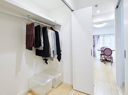 広々としたウォークインクローゼット。たくさんの洋服がかけられたポールの下にはプラスチックケースも置かれている。