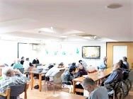 高齢者が集まってレクリエーションに参加している様子。施設内のある日のひととき