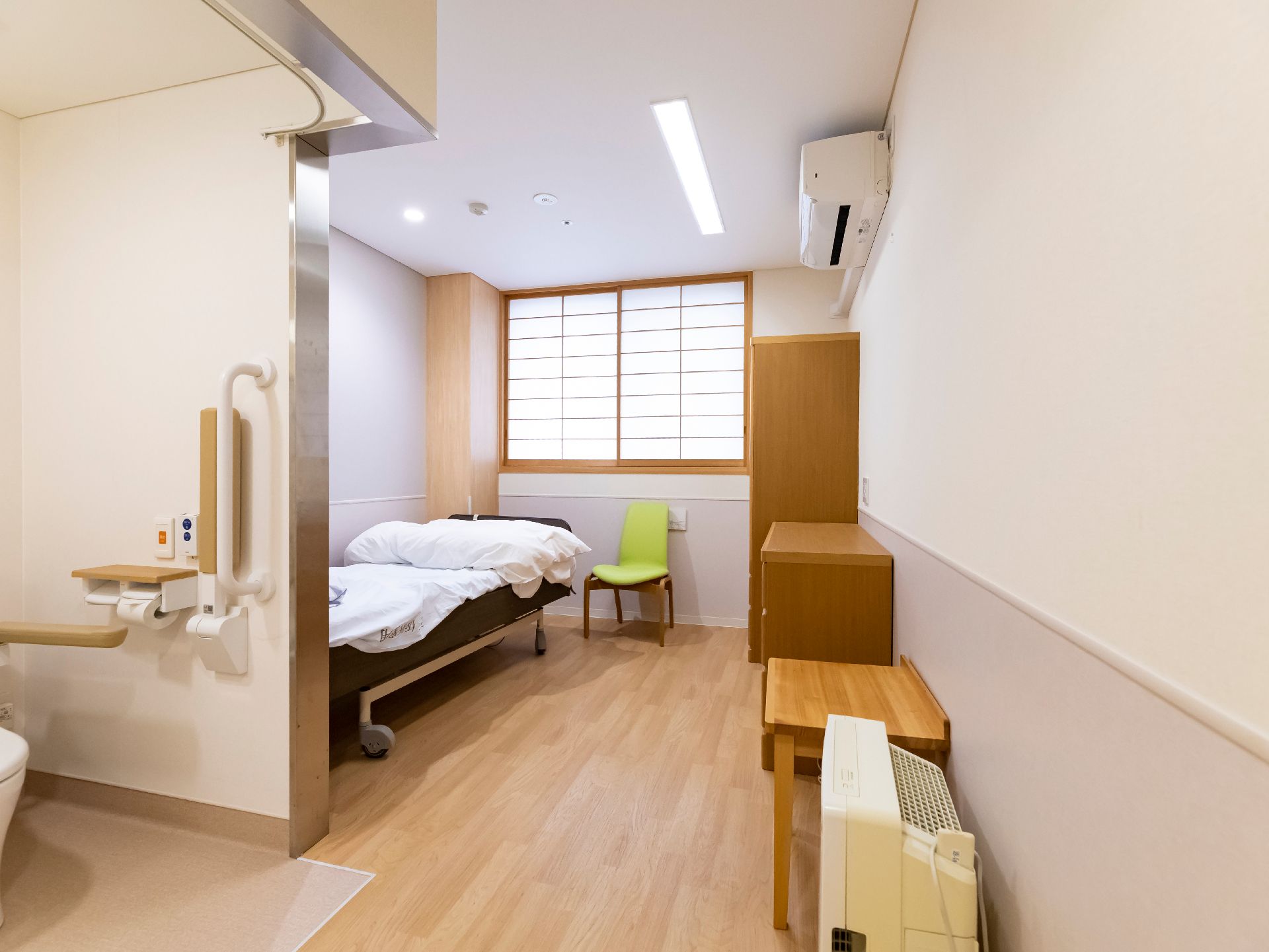 トイレとベッドが壁を隔てて設置されている白い壁の部屋