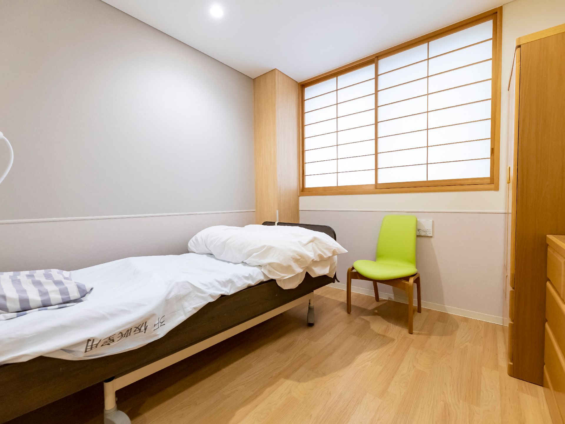 障子に覆われた窓のある部屋の壁沿いに置かれたベッドとライムグリーンの椅子