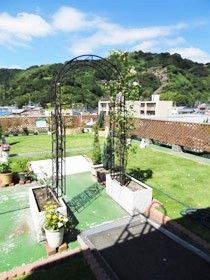 周辺には山山や住宅地があり、屋上には立派なバラのアーチや花が植えられたプランターなどがある。