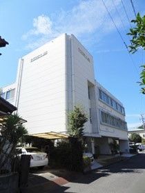 ３階建ての建物は白を基調としていて、周辺には住宅地がある。各フロアには窓がたくさんついている。