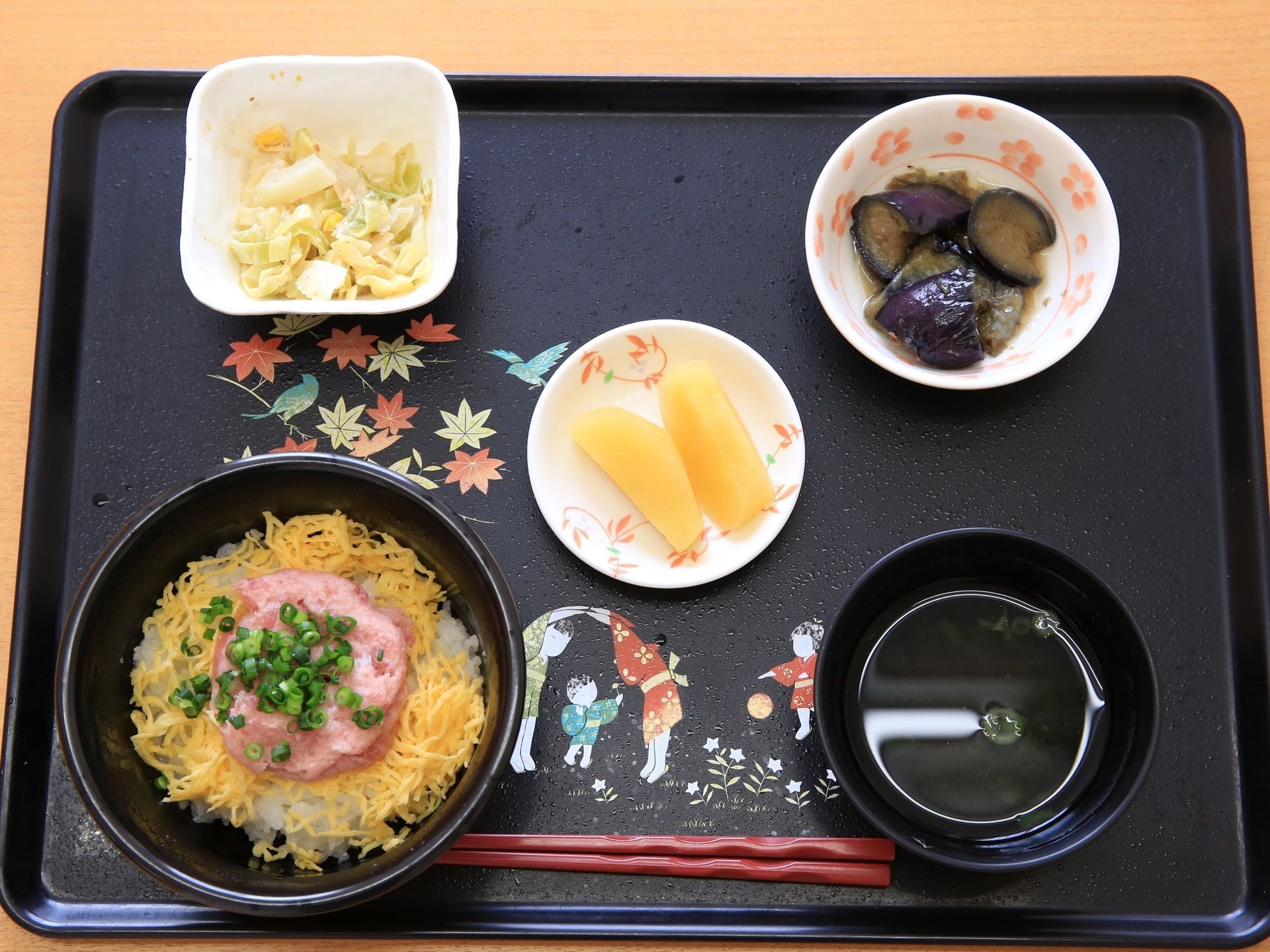 黒いトレーの上には、ご飯のうえに錦糸卵とマグロのタタキをのせた丼物とお吸い物、他にナスの漬物と野菜物など３つの小鉢が並んでいる。