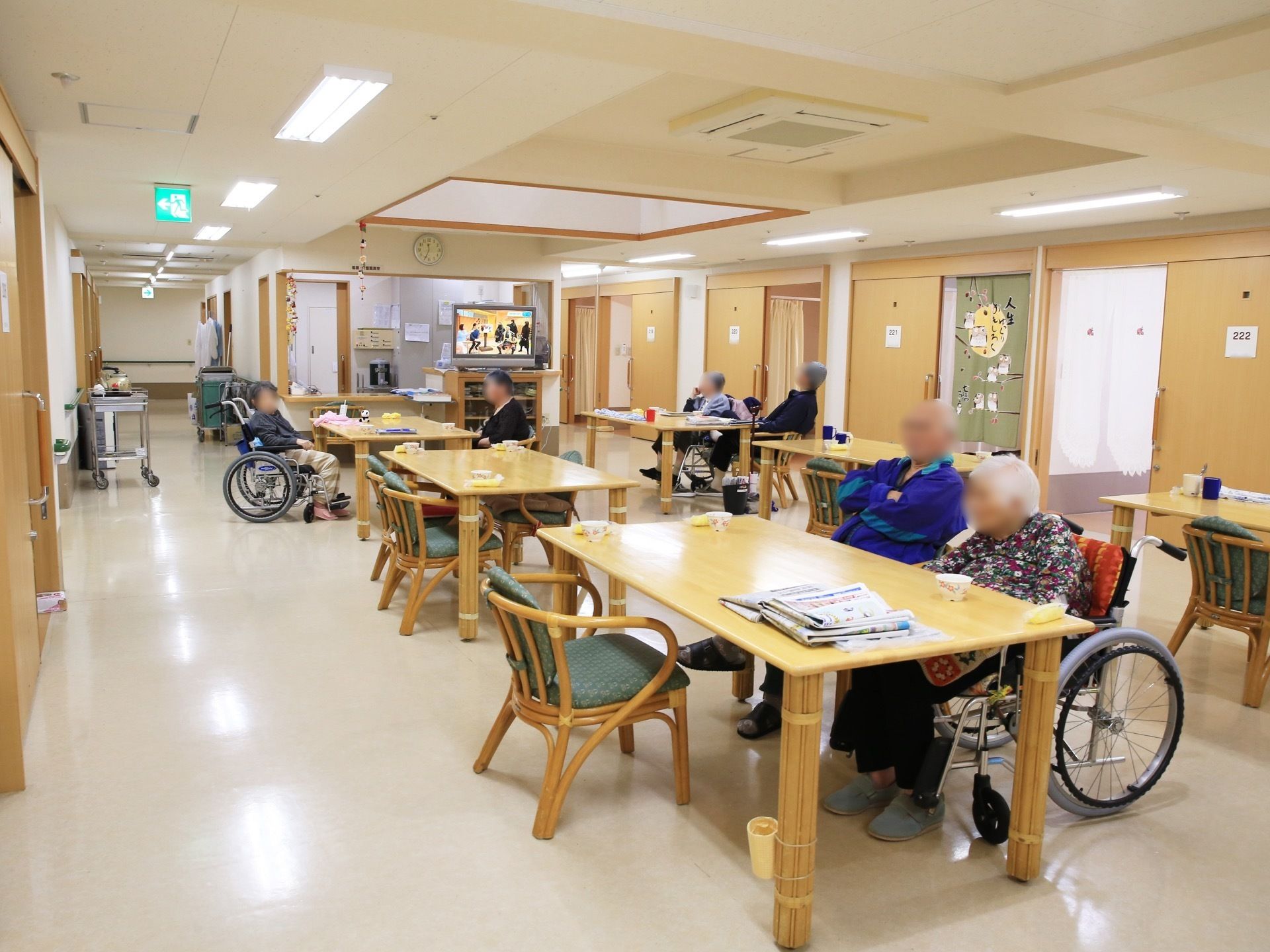 共有スペースに、多くの椅子やテーブルが置かれている。６人の入居者様が、３つのテーブルに分かれて座っている。