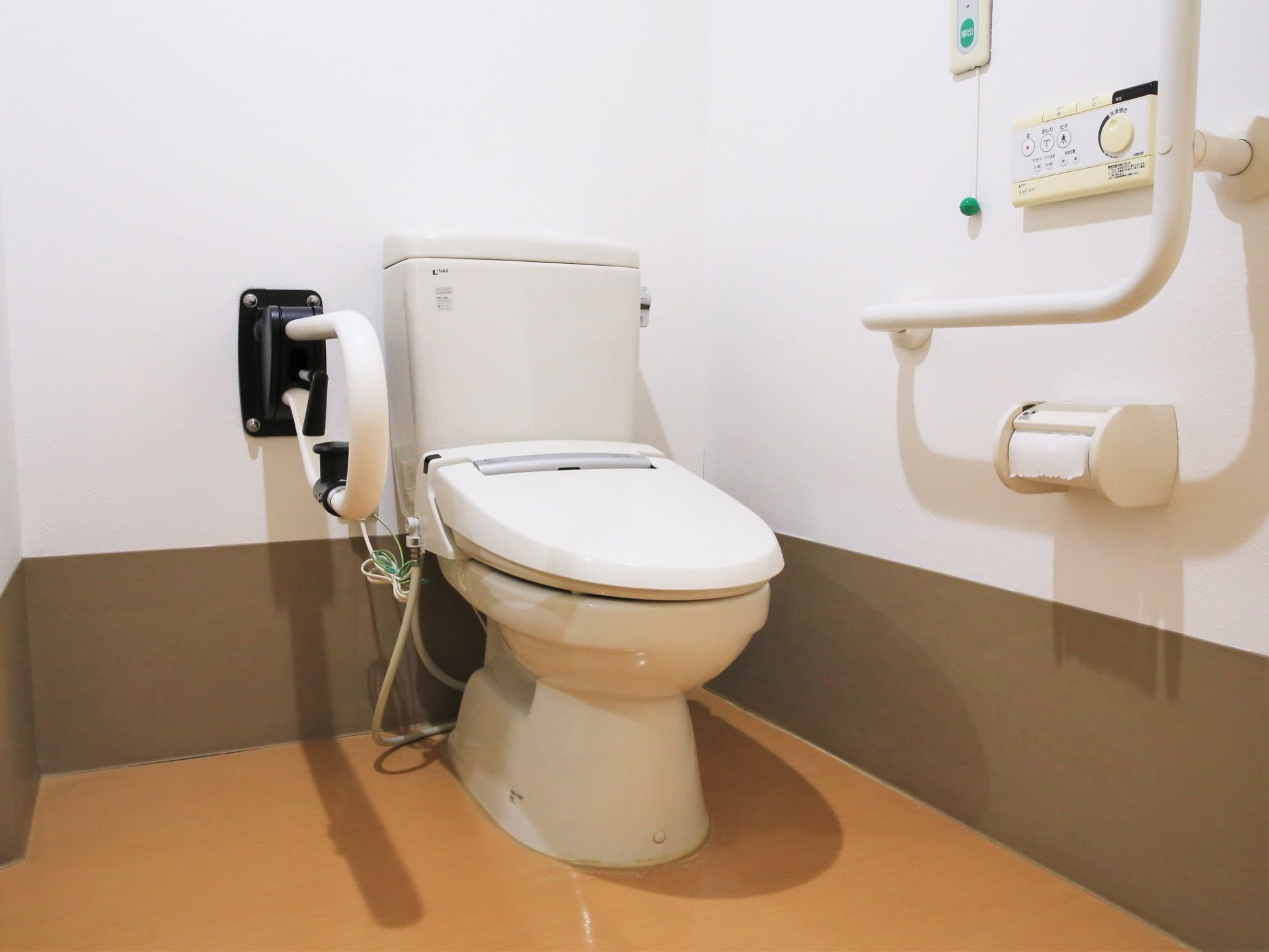 白色、ダーク系の壁紙が貼られたトイレである。洋式の便座を完備している。可動式の手すりも備え付けられている。