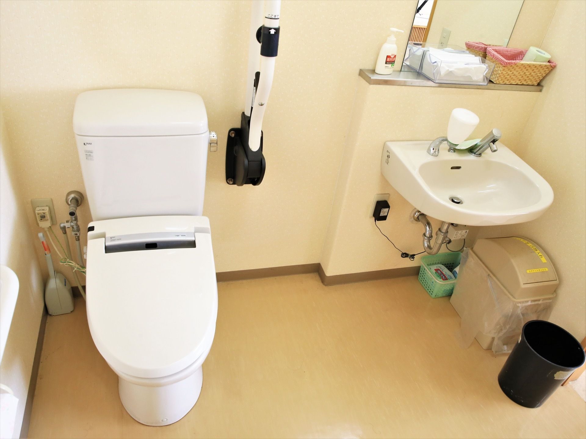 可動式の手すりが完備されたトイレである。そばに手洗い場があり、鏡の下には小物類を置くスペースが設けられている。