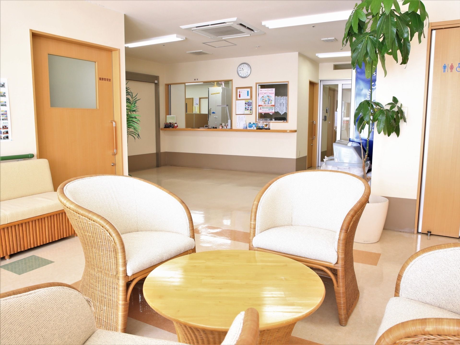 丸形テーブルを囲むように、１人掛けの椅子が配置されている。壁側にもソファが置かれてある。奥にはスタッフルームが見える。