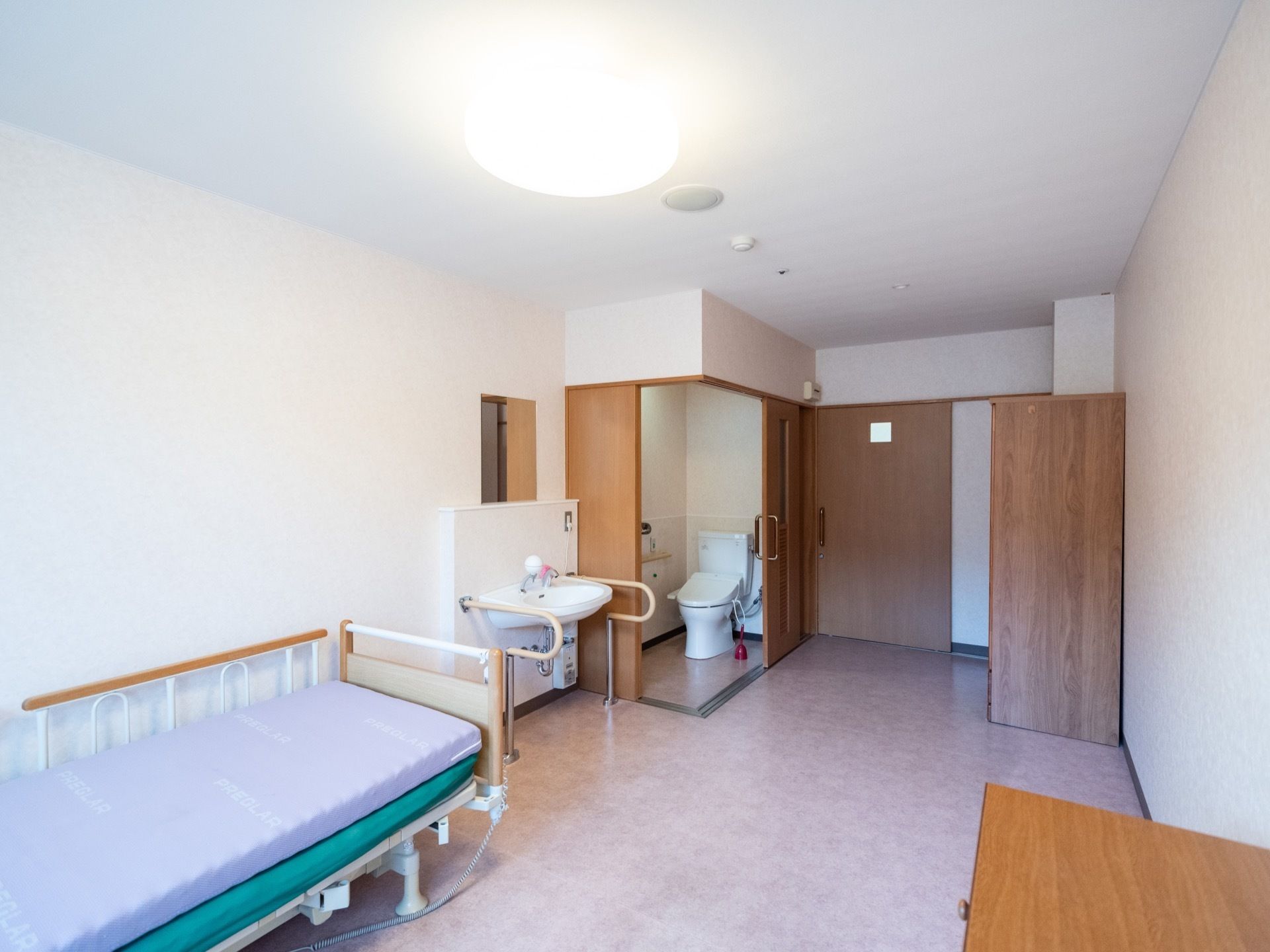 居室の扉はスライドドアになっている。トイレの近くに、手すりがついた車椅子対応の洗面台が設置されている。