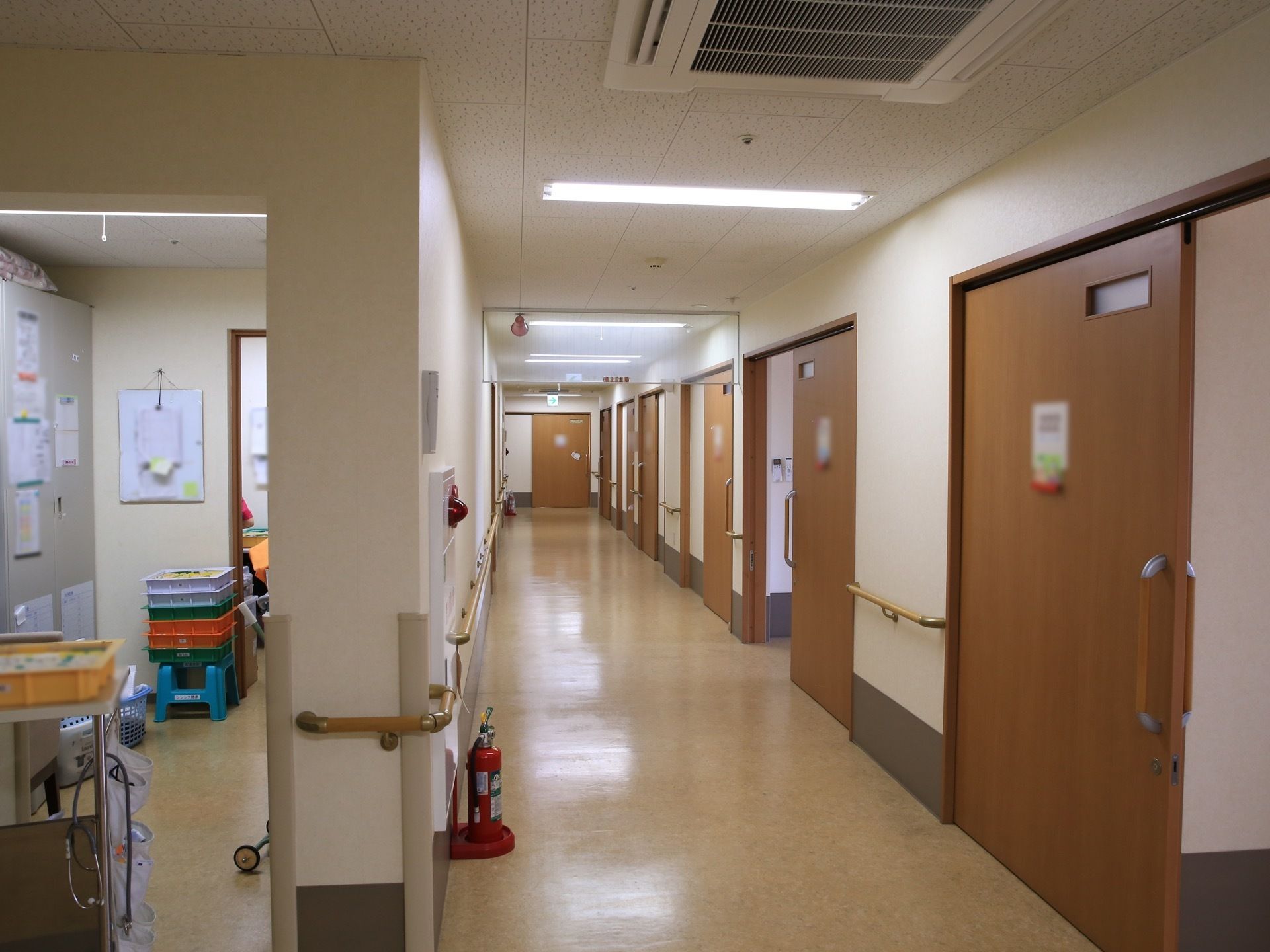 通路の右側には、大きな引き戸が並んでおり、引き戸と引き戸の間の壁には手すりが設置されている。天井には蛍光灯がある。