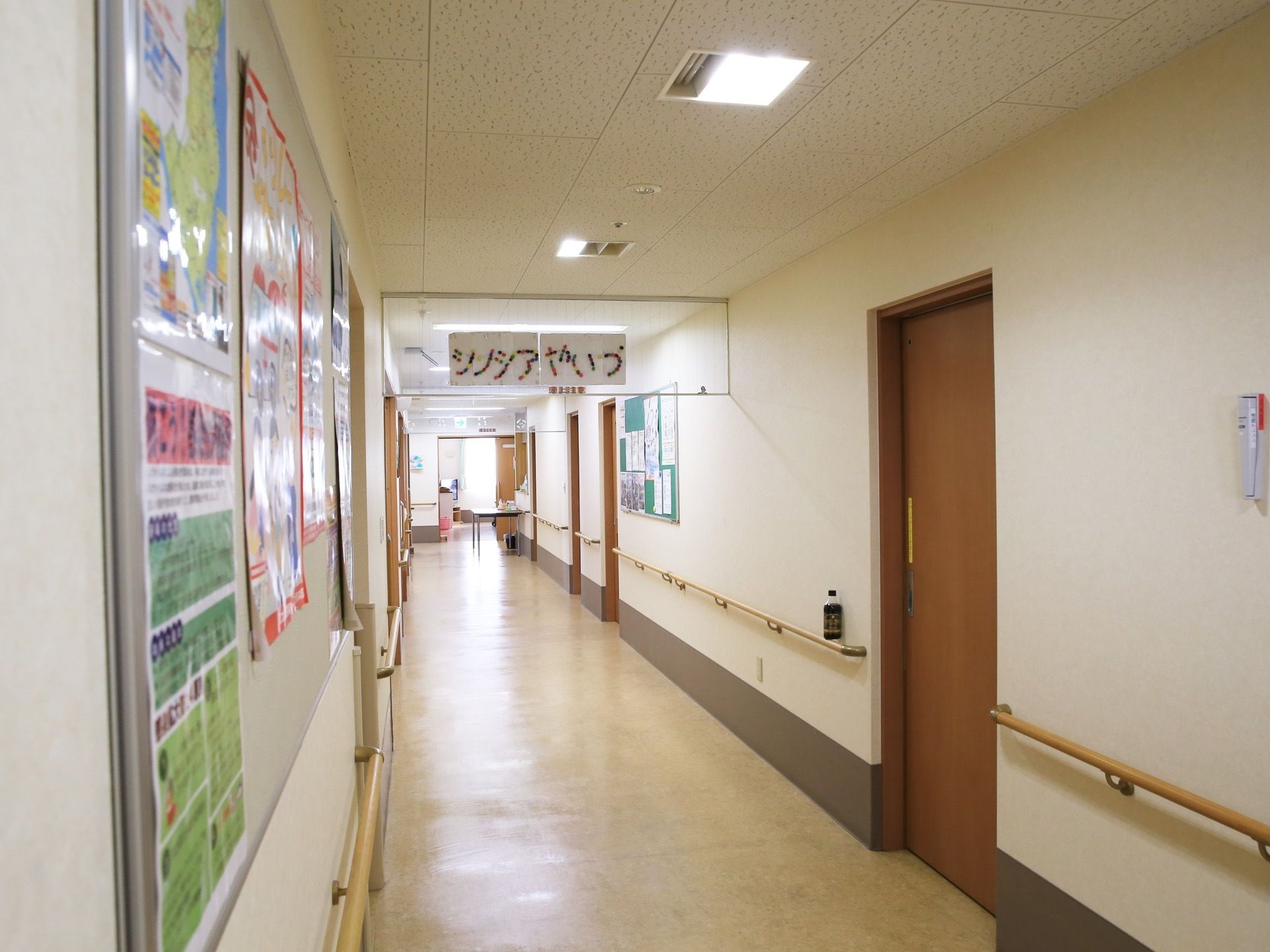 壁の掲示コーナーには、複数の掲示物が貼られており、通路の両壁に手すりが設置されている。手すりの上にのペットボトルの飲み物が置かれている。