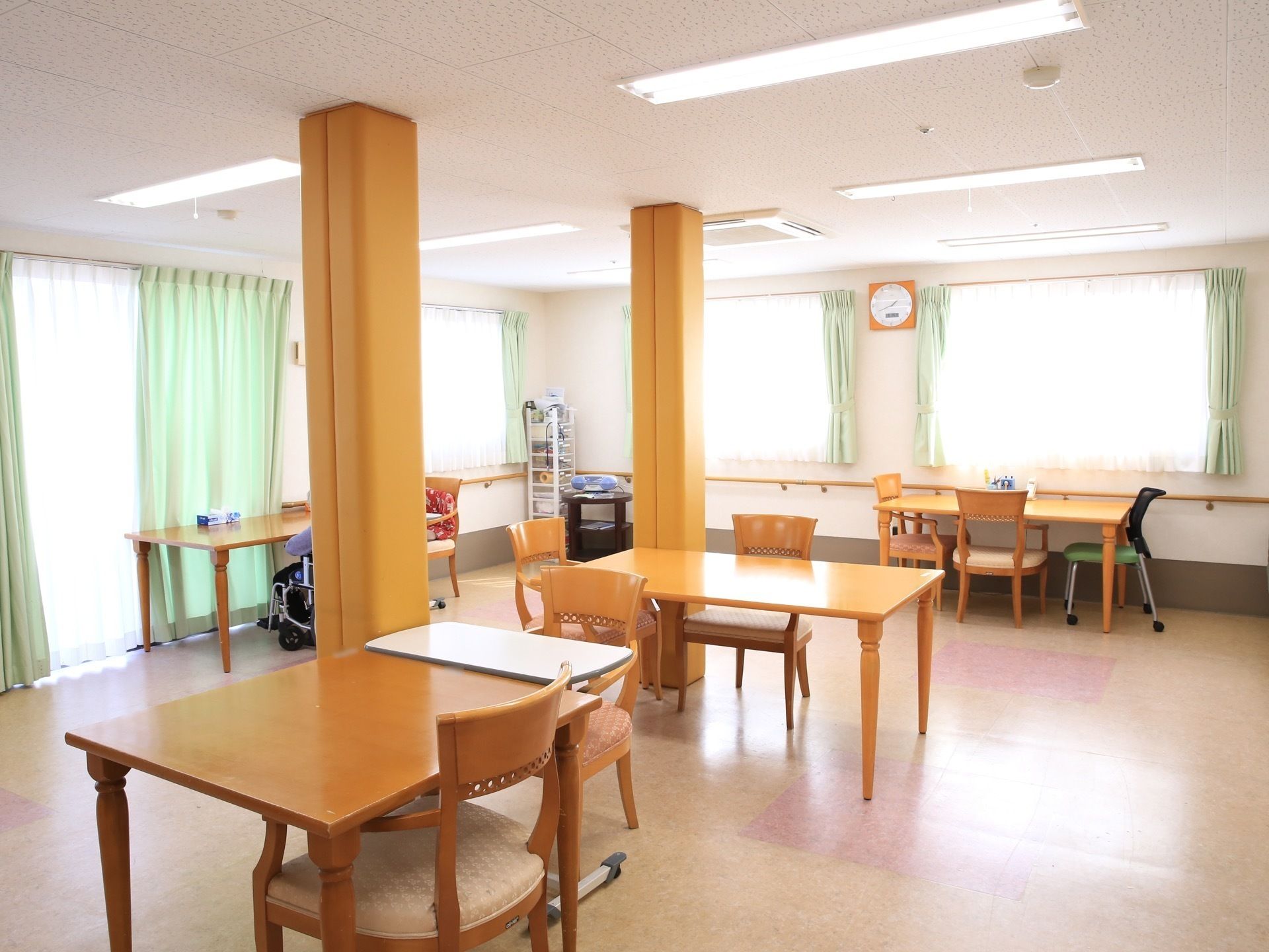 大きな窓から明るい自然光の入るテーブルセットの配置された共有スペース