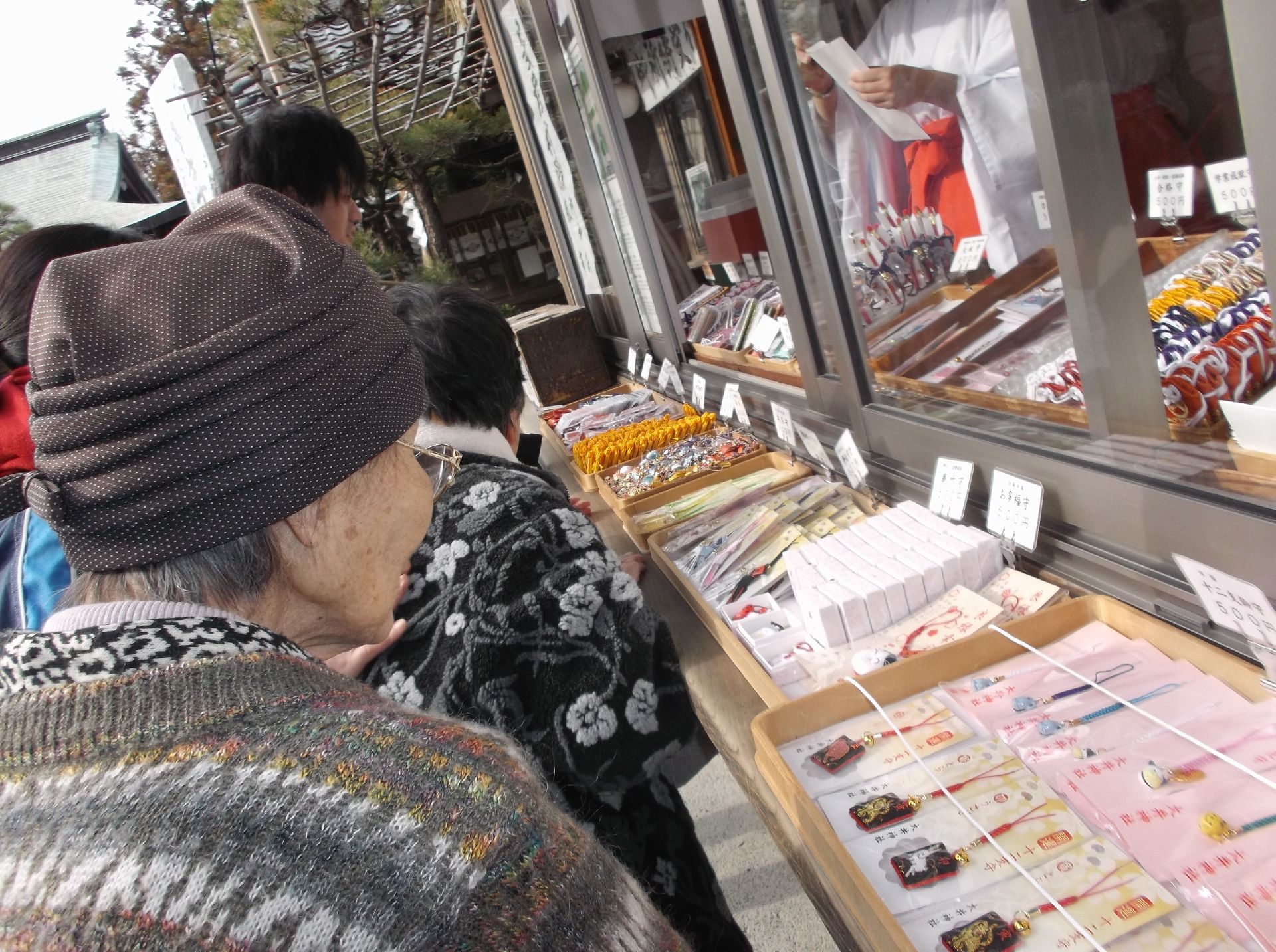 茶色い帽子をかぶった高齢者が神社のお守りを見ている。