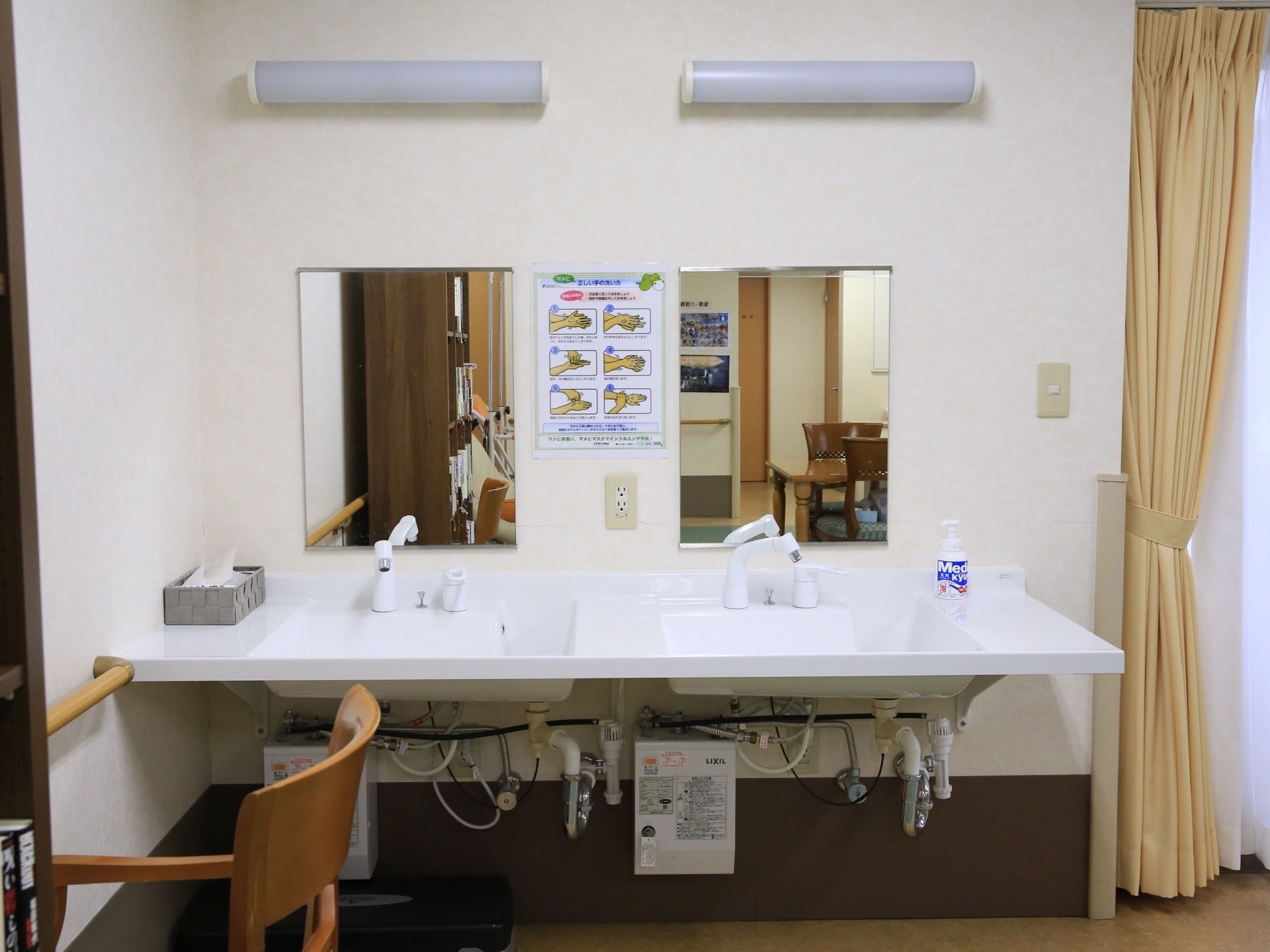 洗面台が2つ並んでいる。壁面に四角い鏡が2つ並べて設置されており、その間に手洗いの方法が記されたポスターが掲示されている。