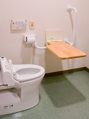 木製の可動式のバーが付いたトイレ。呼び出しボタンが付き、便座にはふたがない。