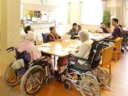 たくさんの入居者がテーブルに集まり、スタッフとレクリエーションを楽しんでいる様子。
