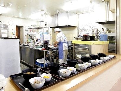 衛生帽やマスク、エプロンなどをしたスタッフがていねいに料理を盛り付けている様子。