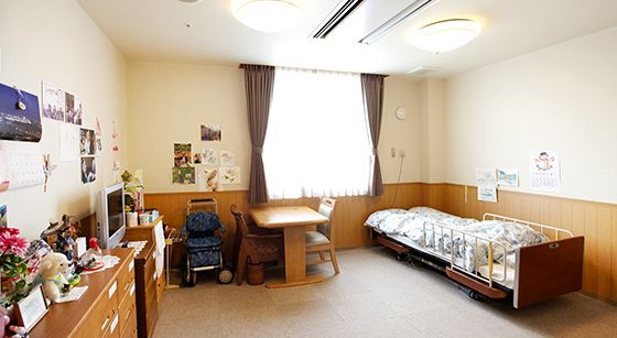 広々とした居室は寝具付きベッドやタンスなどの家具付き。大きな窓にはレースカーテンとカーテンが付いている。