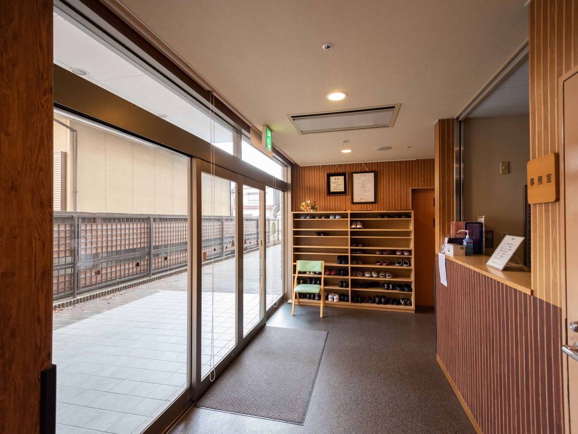 間口広く、両開きのガラスサッシの扉が設置されている玄関である。木目調を施した受付カウンターが設けられている。