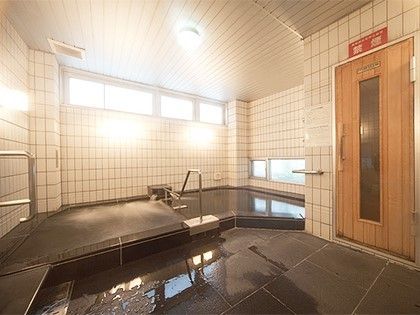 大きな浴槽には手すりが付き、右側にはサウナへと続く木製の扉があり、その上には「禁煙」と書かれた看板がある。