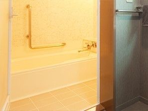 白い浴槽が設置された浴室はシンプルで洗い場も広い。エル字型の手すりが設置されている。