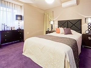 大きなベッドが置かれた寝室は窓も大きく明るい。ベッドの上にはエアコン、周りには収納家具がある。