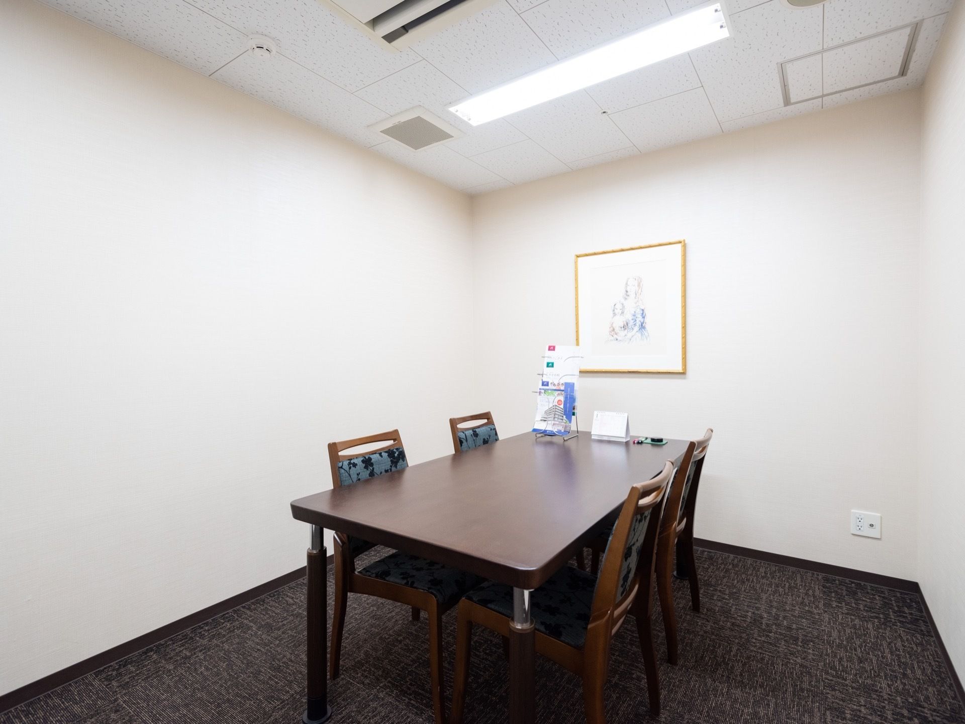 相談室はほどよい広さで、中央には花柄の椅子が４脚とテーブルが置かれている。床には、ダークグレーのカーペットが敷かれている。
