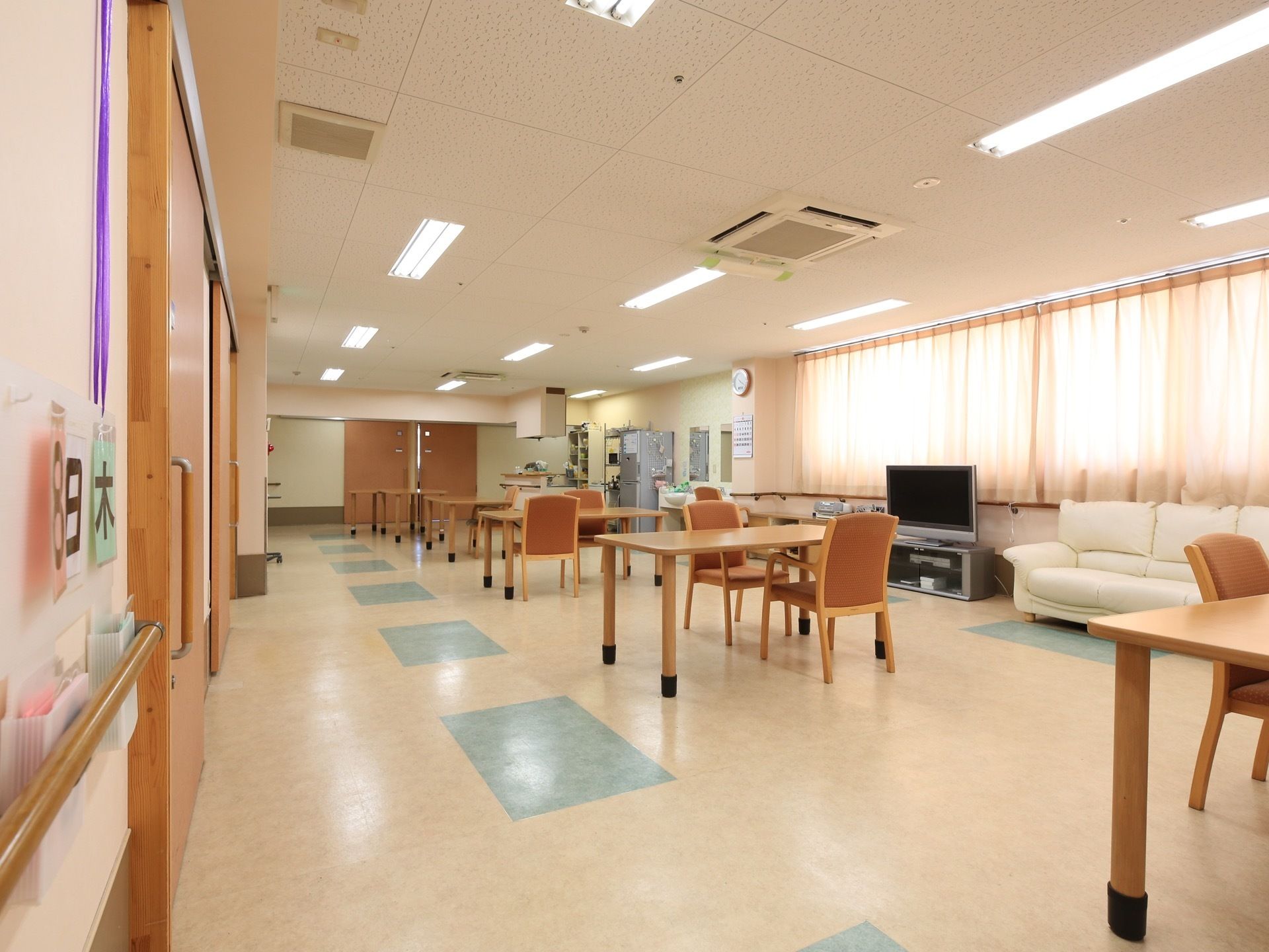 広々として開放的な共同生活室は、部屋の中央にテーブルが並んでいる。通路を広く確保して、スムーズに通行できるようにしている。