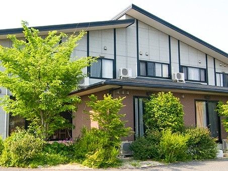 緑に囲まれた2階建ての建物は１階部分がブラウン、２階部分が白で三角屋根が付いている。