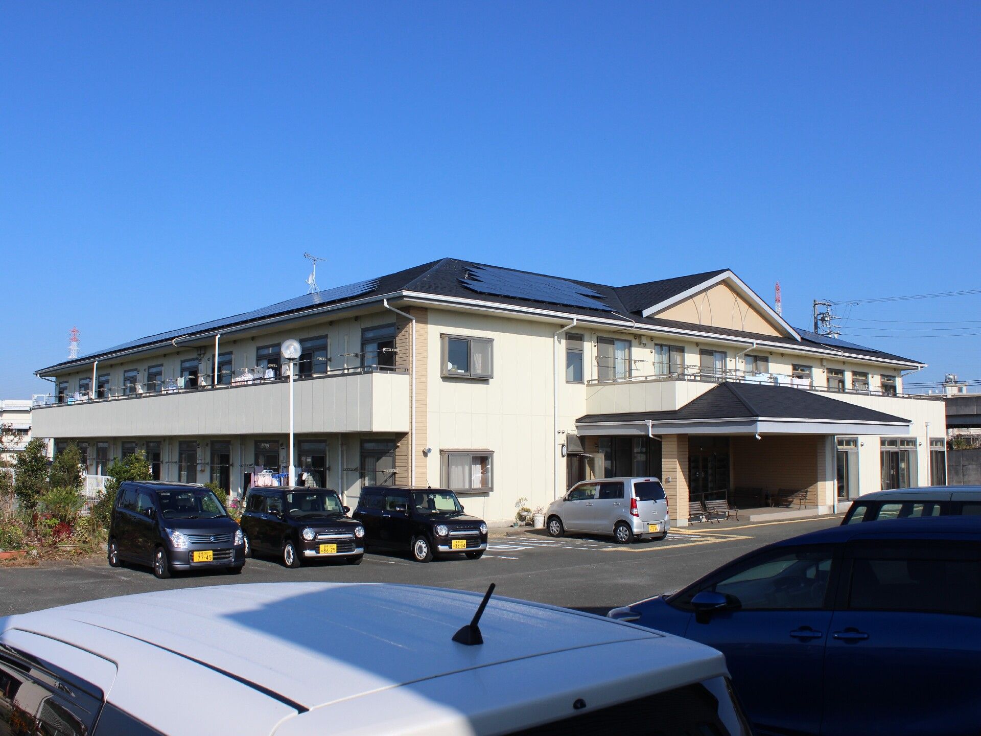 ２階建ての建物は屋根が付き、外壁は白っぽい色で明るい雰囲気。広い敷地内には駐車場もあり、たくさんの車が止まっている。
