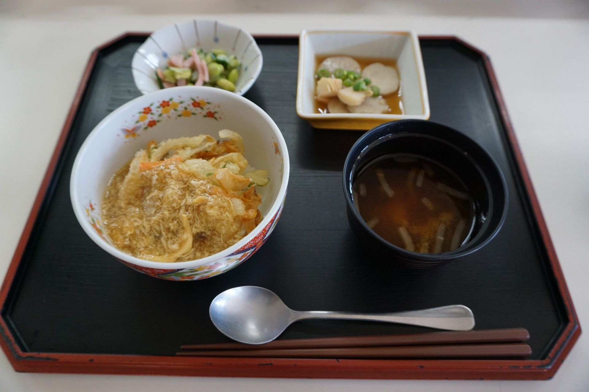 福神漬けが添えられたカレーライスに汁物、あえ物などが並べられた黒いトレーには、スプーンと箸が置かれている。