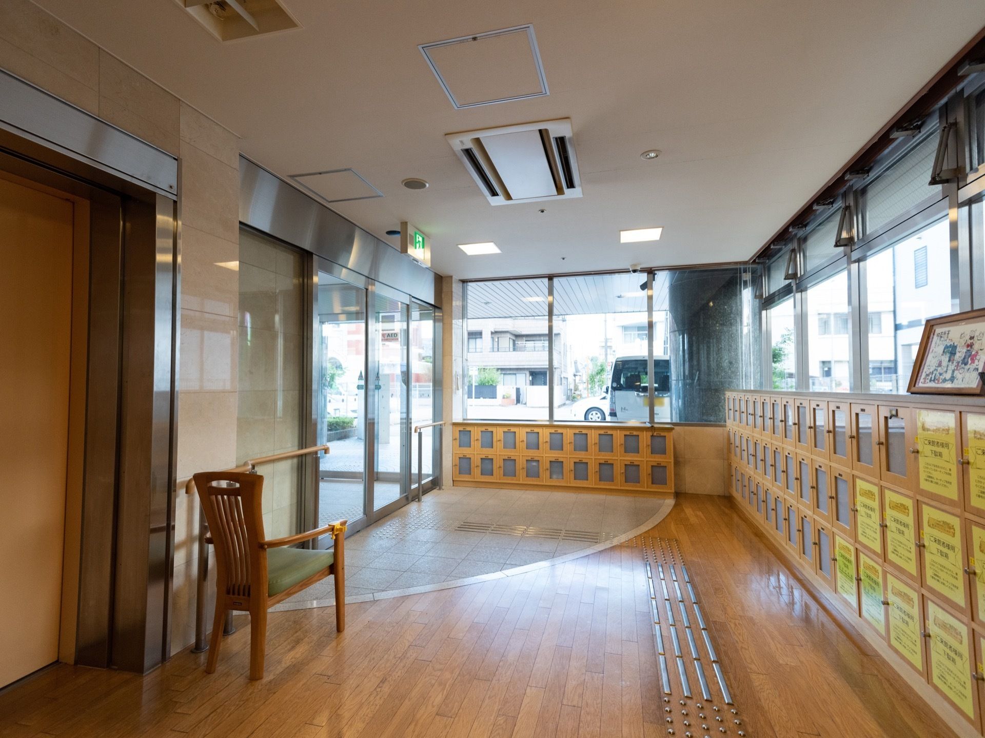 大きな自動ドアがあり、その横には手すりが設置され、椅子も置かれている。周囲の壁には多数の下駄箱がある。