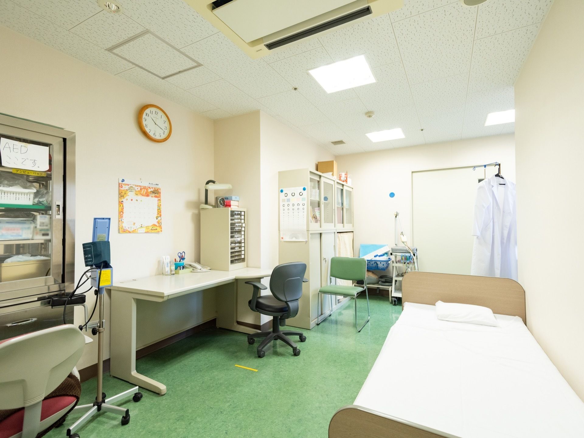 デスクとベッドなどが設置されていて、血圧を測る道具や白衣のかけられたハンガーラックなども置かれている。