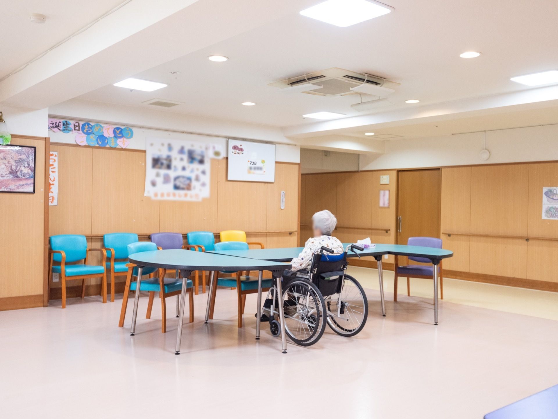 白い床と天井に木目調の壁で、明るい食堂スペースである。壁面には写真や飾りを貼り、テーブルと椅子が置かれている。