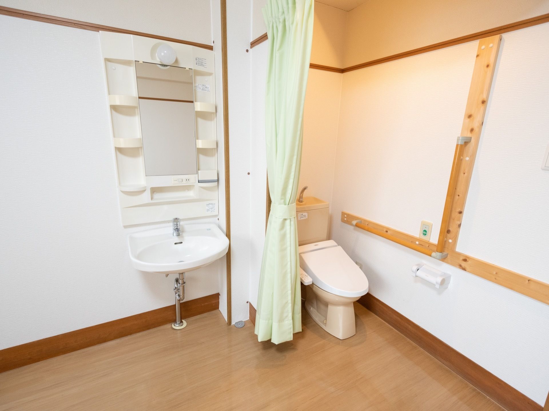 白い壁に木目調の床のゆとりのある空間に、カーテンで仕切られたトイレと足元がフリースペースになっている洗面台が設置されている。