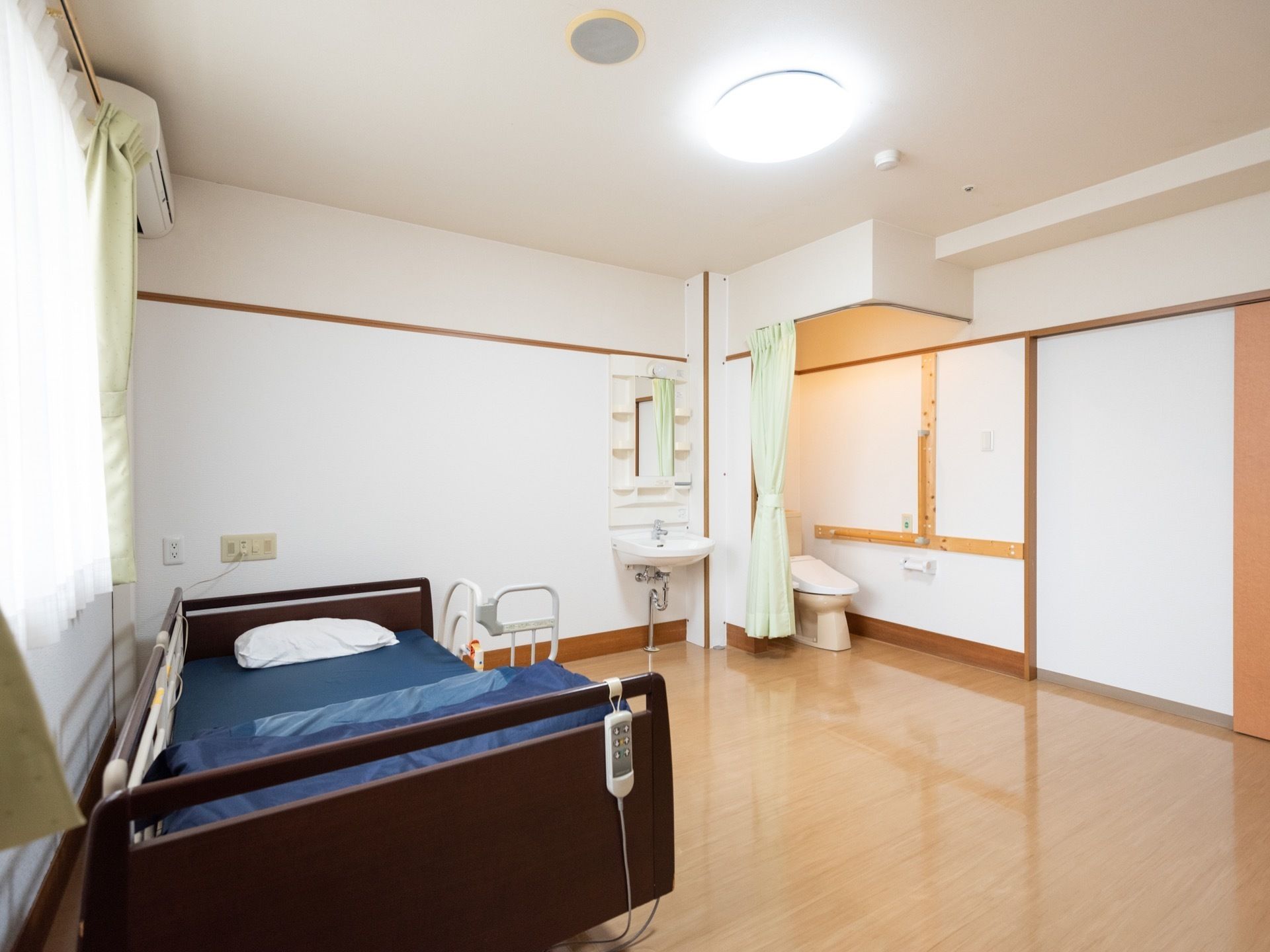 白い壁に、綺麗に磨かれた木目調の床の居室である。洗面台とカーテンで仕切れるトイレが備え付けられている。