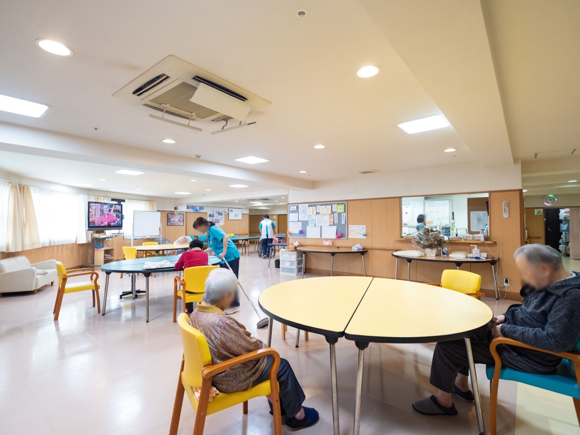 奥行きのある食堂である。半円のテーブルと椅子が置かれ、テーブルは並べると円になる。空調にはルーバーがついている。