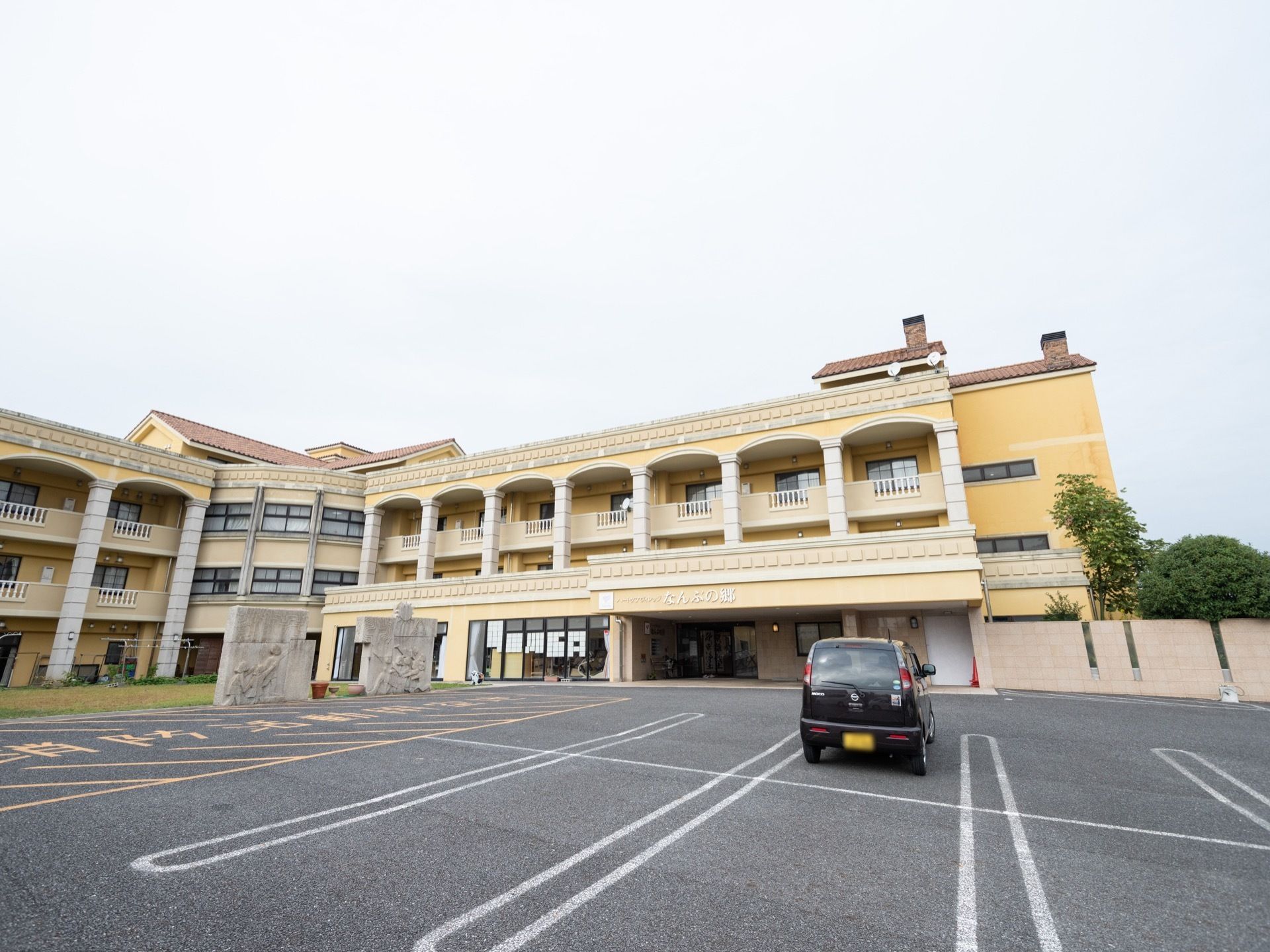 クリーム色やオレンジ、黄色などの外壁を使ったホテルを思わせる施設外観である。玄関手前は広く開放的な駐車スペースが広がる。