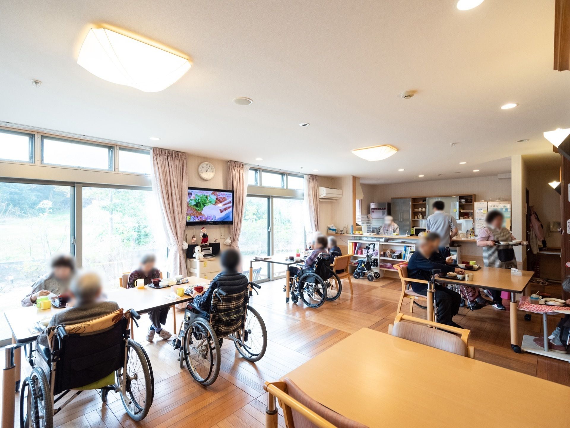 大きな窓から外光が差し込む食堂で、食事やテレビを楽しむ入居者様