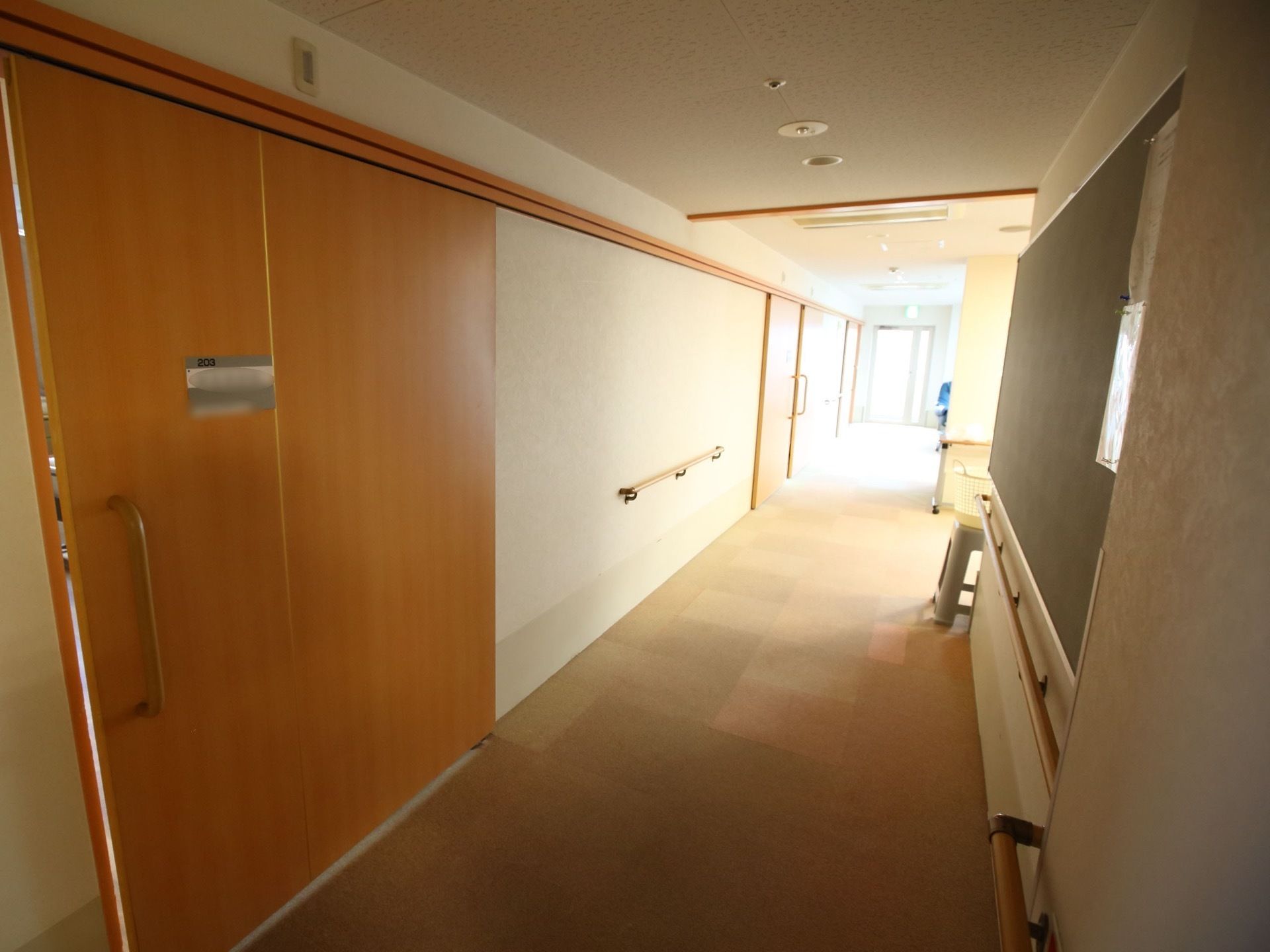 廊下の左右の壁には、掴まっていただける手すりがある。奥に設置されている窓から明るい日差しが差し込んでいる。